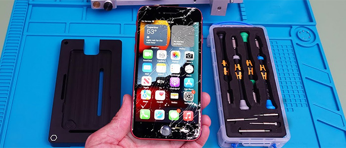 A hand holds a red iPhone with a badly shattered screen next to a professional toolkit and repair mat, demonstrating that C&C Cell Phone & Computer Repair offers quick screen replacement in the St. Louis area.