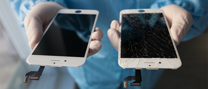 A technician, wearing gloves and a blue coat, holds up two separate iPhone screens, contrasting a brand-new screen (left) with a completely shattered one (right), emphasizing the quality screen repair offered by C&C Cell Phone & Computer Repair in the St. Louis area.