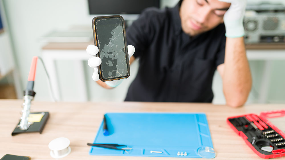 A C&C Cell Phone & Computer Repair technician holds up a device with a severely cracked screen, ready to provide fast and trustworthy repair services in the St. Louis area.
