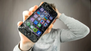 A frustrated user holds up a smartphone with a completely shattered screen, highlighting the fast and affordable repair services available from C&C Cell Phone & Computer Repair in the St. Louis area.